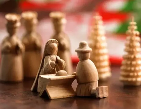 Una escena del nacimiento de madera bellamente elaborada que presenta a María y José junto a un pesebre, con figuras de madera de los Tres Reyes Magos y árboles de Navidad en el fondo, evocando el espíritu navideño | Ile Tours